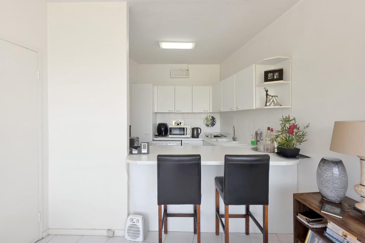 A compact kitchen featuring white cabinetry, a tiled backsplash, and a functional breakfast bar area, providing efficient workspace and casual dining options.