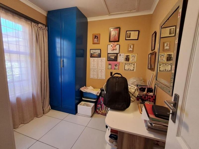 A functional bedroom featuring tiled flooring, a built-in blue wardrobe, and a window with security bars, offering a practical space for rest or study.