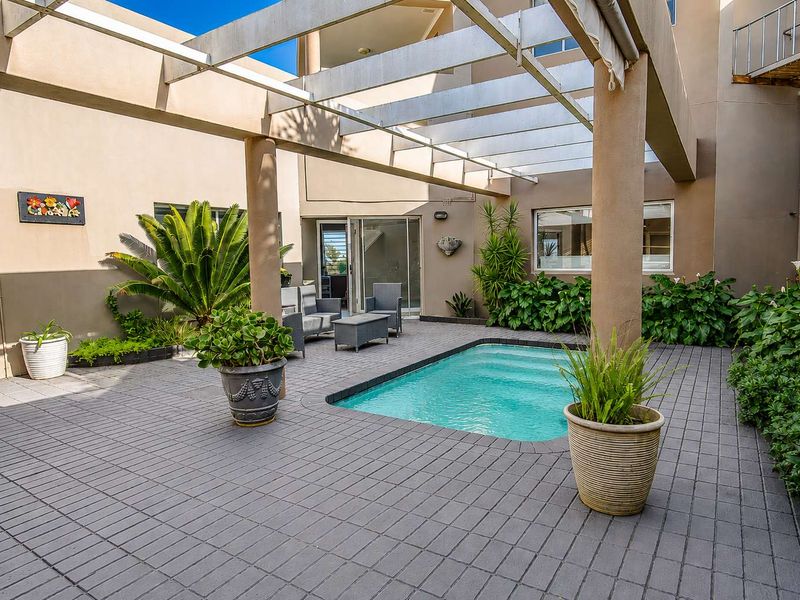 A well-maintained courtyard featuring a swimming pool, paved patio area, and a structural pergola providing partial shade.
