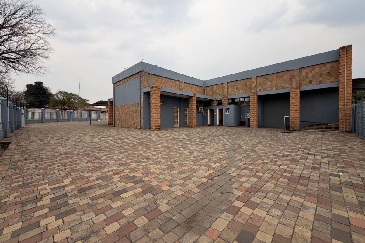 Rear exterior view of a commercial property featuring a large paved yard, stone-clad facade, and roller shutter access.