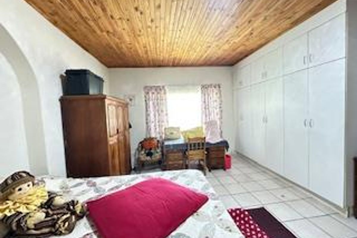 A bedroom featuring built-in cupboards, tiled flooring, and a wooden panelled ceiling.