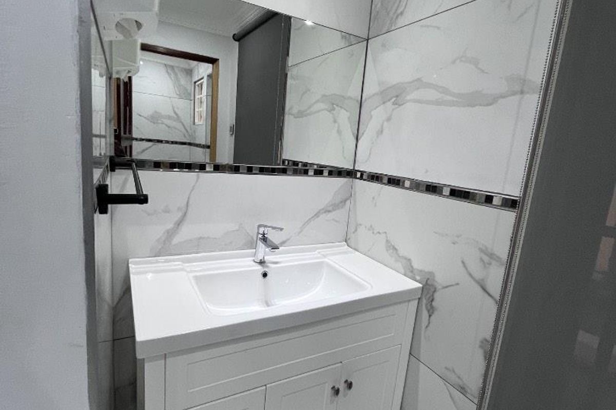 Modern bathroom featuring a white vanity cabinet with integrated sink, large wall mirror, and marble-effect wall and floor tiling.