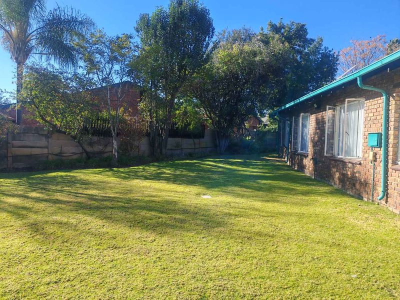 A spacious rear garden featuring a well-maintained lawn, mature trees, and a brick exterior facade with functional guttering.
