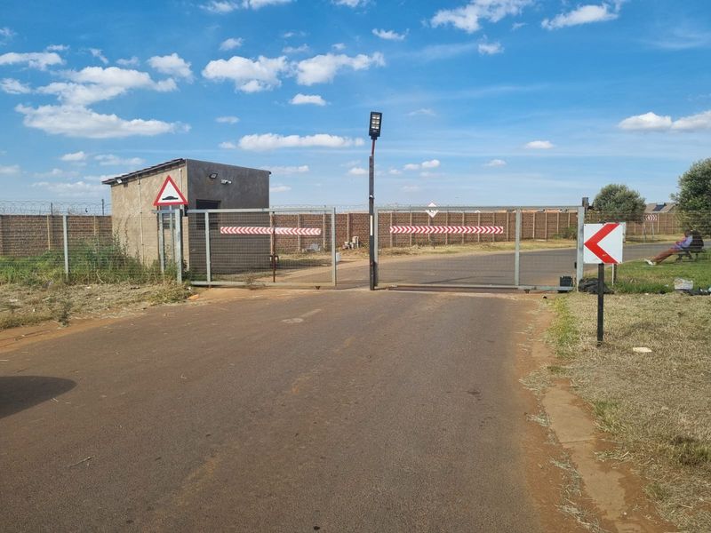 Entrance to the property featuring a security gate, guard house, and perimeter wall with razor wire fencing.