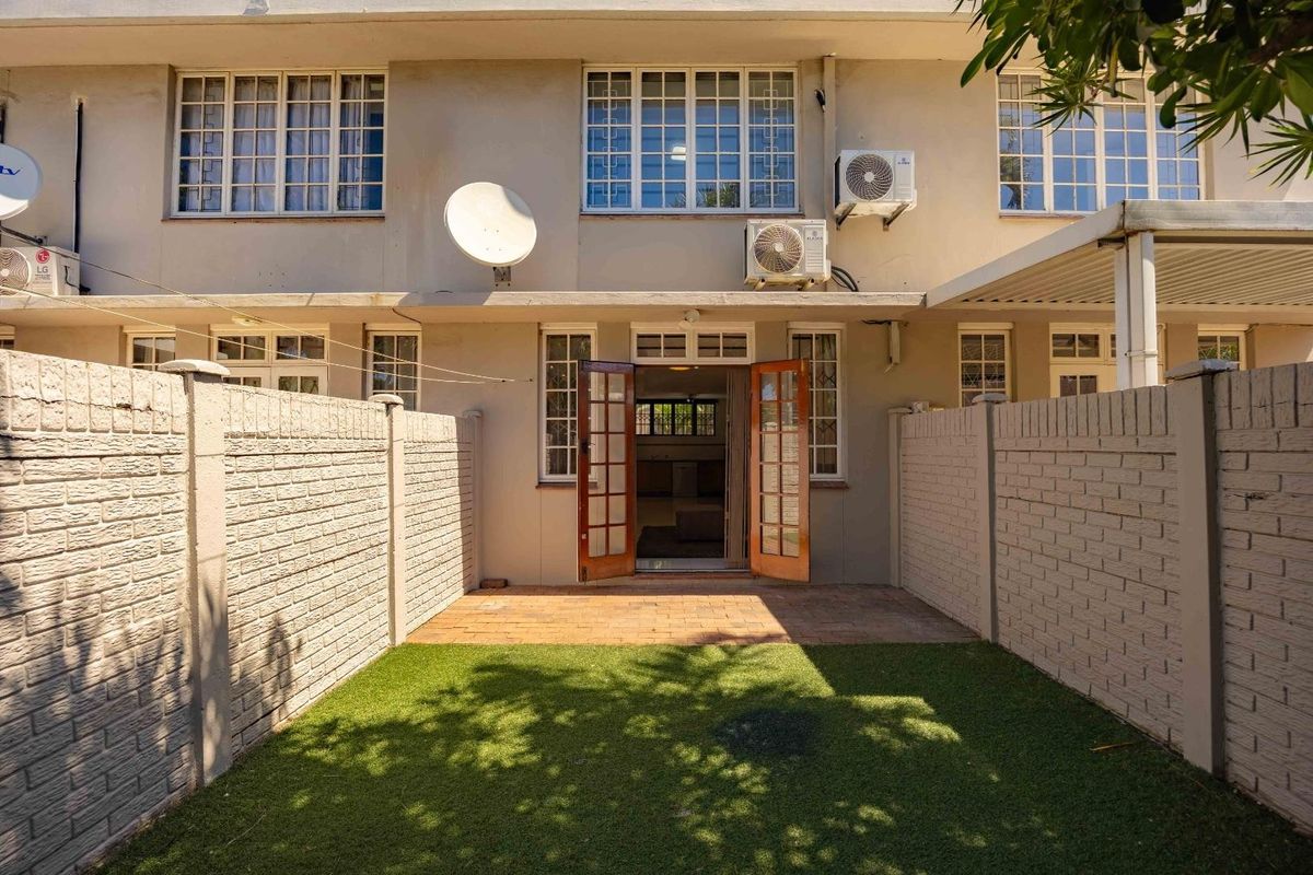 Rear exterior view of the townhouse featuring a private courtyard with a paved patio, artificial lawn, and secure brick boundary walls.
