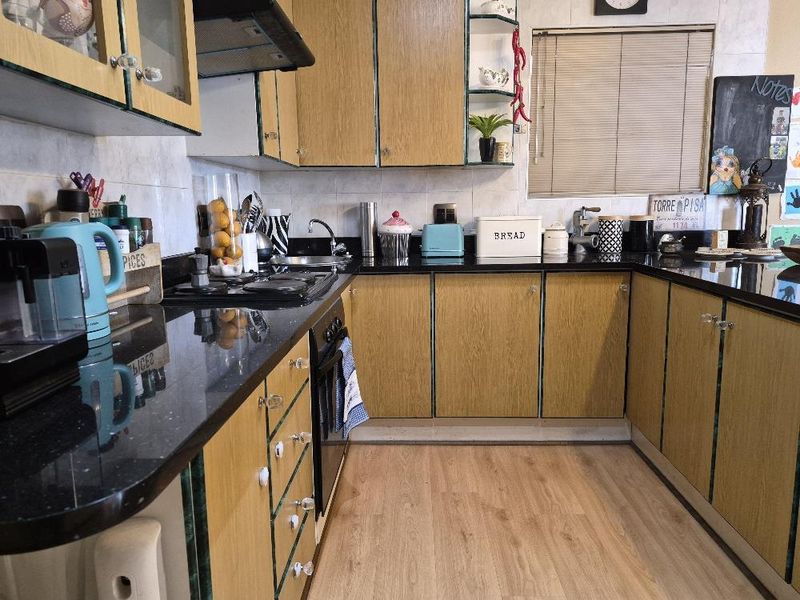 A functional kitchen featuring wood-look laminate cabinetry, black granite countertops, a built-in oven, gas hob, and a tiled backsplash.