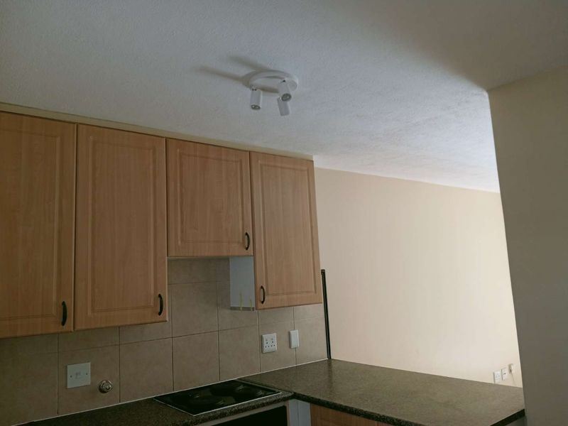 A compact kitchen area featuring laminate cabinetry, a tiled backsplash, and an integrated electric hob, currently showing a missing cabinet door.