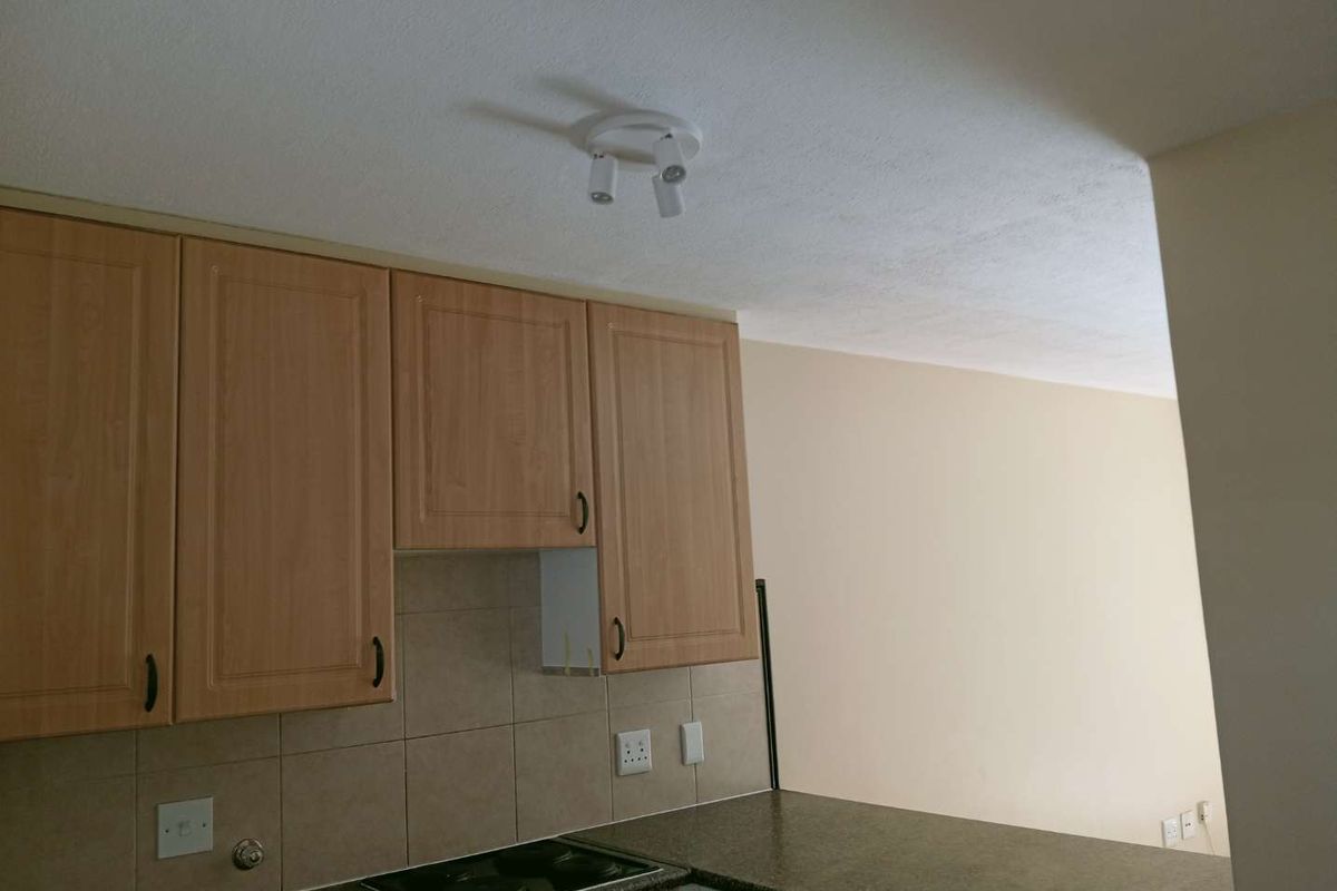 A compact kitchen area featuring laminate cabinetry, a tiled backsplash, and an integrated electric hob, currently showing a missing cabinet door.