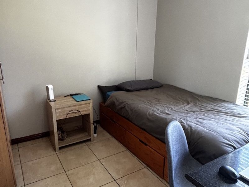 A functional bedroom featuring neutral wall tones, tiled flooring, and a window with fitted blinds.