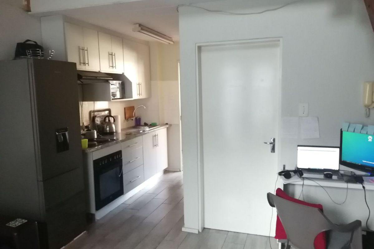 A functional kitchen area featuring built-in cabinetry, an integrated oven and hob, and tiled flooring, adjacent to a workspace area.