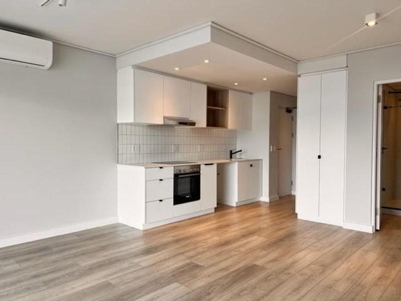 Modern open-plan kitchen featuring sleek white cabinetry, integrated appliances, tiled backsplash, and light wood-look laminate flooring in a bright, well-maintained living space.