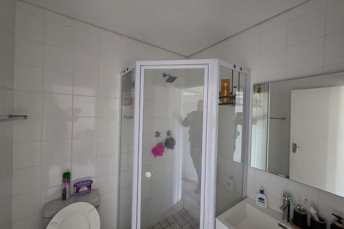 A functional bathroom featuring a corner shower enclosure, a wall-mounted vanity with a basin, and white wall tiling.
