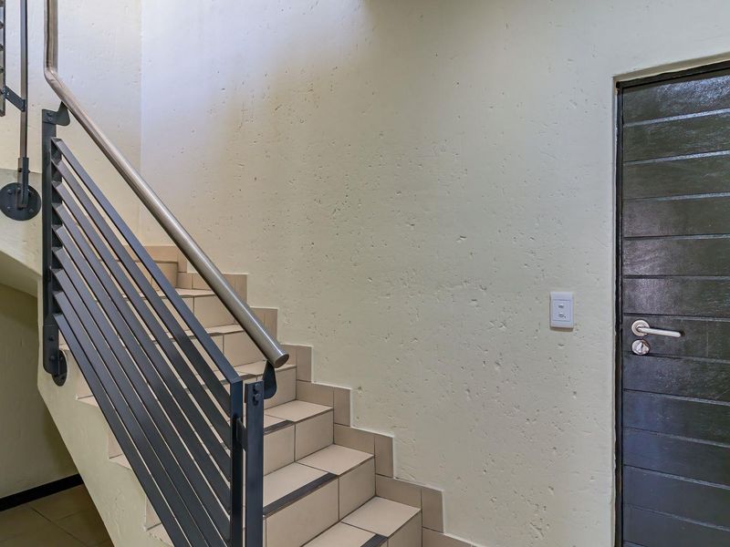 A functional interior hallway featuring a tiled staircase with a modern metal balustrade and a solid internal door.