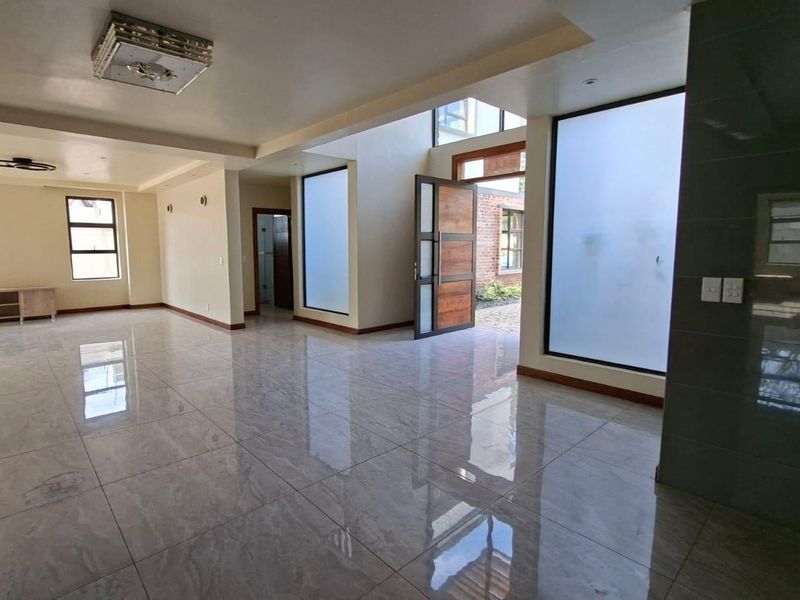 Spacious, open-plan living area featuring polished tiled flooring, high ceilings, recessed lighting, and large frosted glass panels providing natural light.