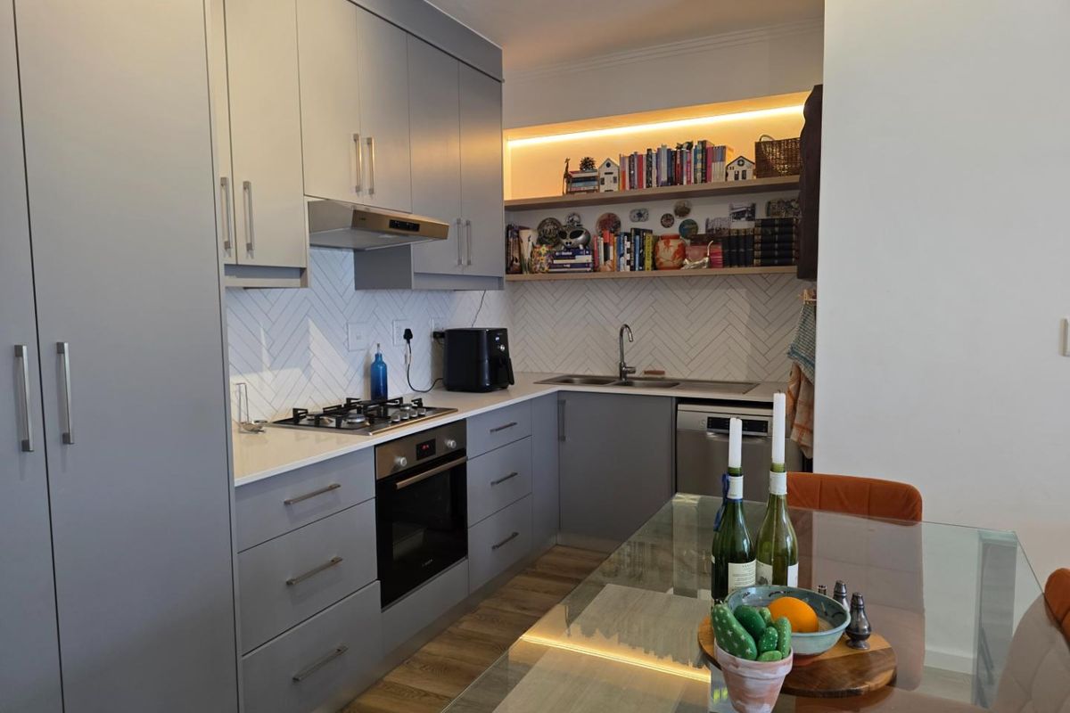 Modern kitchen featuring grey cabinetry, herringbone tile backsplash, gas hob, built-in oven, and integrated shelving with ambient lighting.