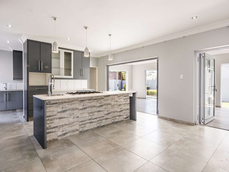 Modern open-plan kitchen featuring a stone-clad island, gas hob, sleek cabinetry, and seamless flow to the outdoor patio through bi-fold doors.