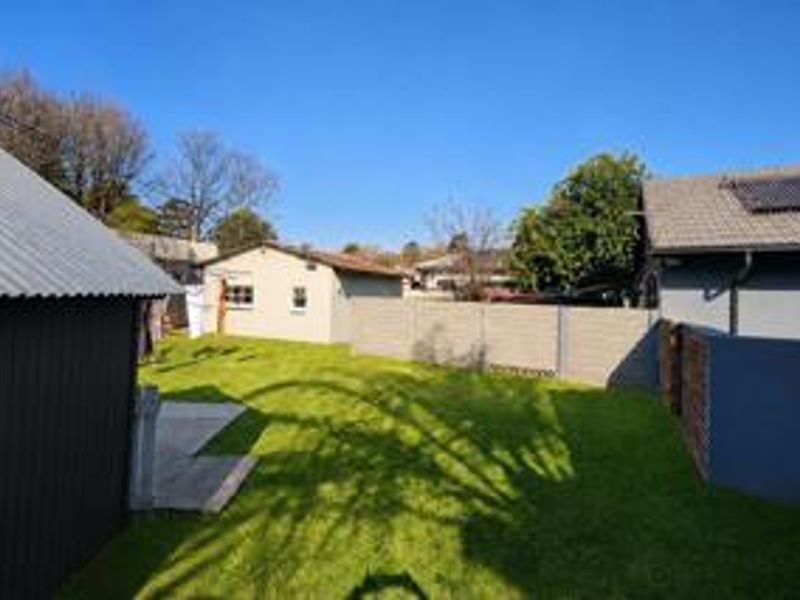 A spacious rear garden featuring a well-maintained lawn, concrete boundary walls, and views of the surrounding property structures and rooflines.