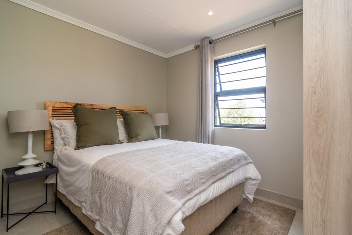 A well-maintained bedroom featuring neutral wall tones, a louvered window for ventilation, recessed lighting, and a built-in wardrobe.