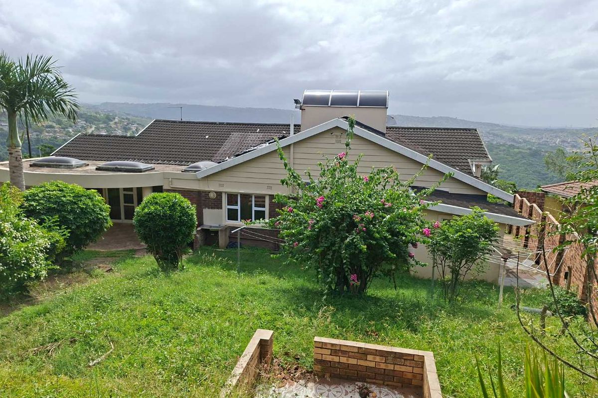 Rear view of the house featuring a tiled roof with solar water heating system, brick masonry, and a sloped garden area.