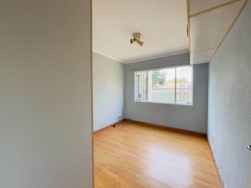 A vacant bedroom featuring laminate flooring, built-in cupboards, and a window with security bars, offering a clean canvas for personalization.