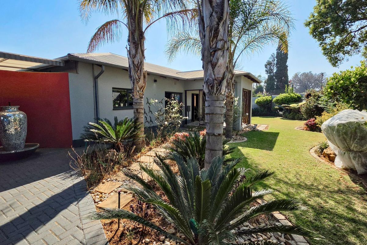 A well-maintained rear garden featuring a paved patio area, established palm trees, and a lush lawn, providing a pleasant outdoor living space.