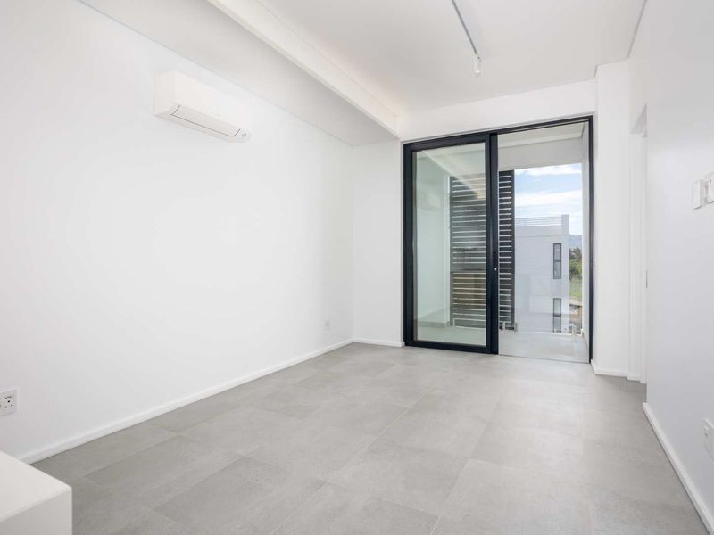 A bright, empty bedroom featuring modern grey tiled flooring, a wall-mounted split-system air conditioner, and a sliding glass door leading to an outdoor area.