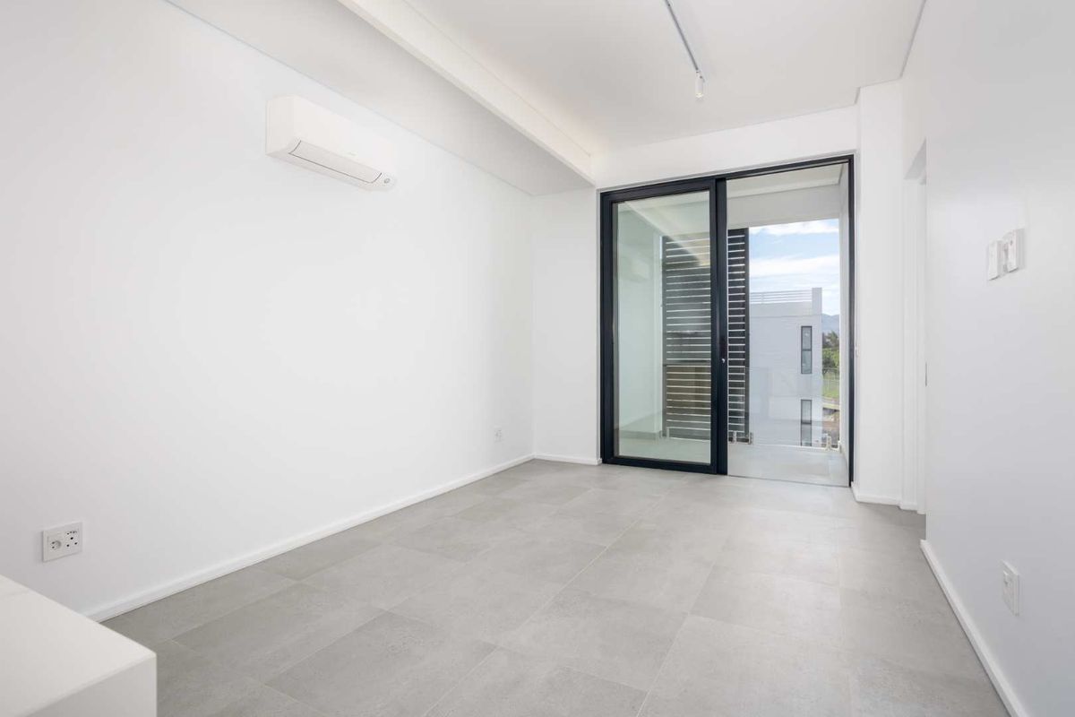 A bright, empty bedroom featuring modern grey tiled flooring, a wall-mounted split-system air conditioner, and a sliding glass door leading to an outdoor area.