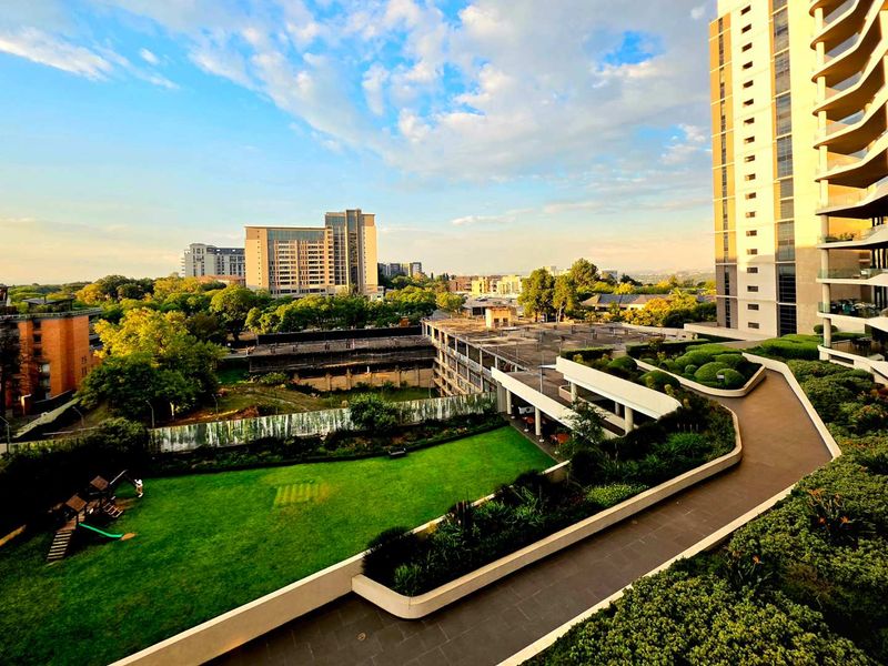 Elevated view overlooking the landscaped communal gardens, paved walkways, and surrounding urban skyline from the penthouse level.