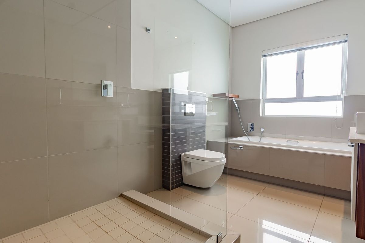 Modern bathroom featuring a glass-enclosed shower, wall-mounted toilet, and a built-in bathtub with neutral tiling throughout.