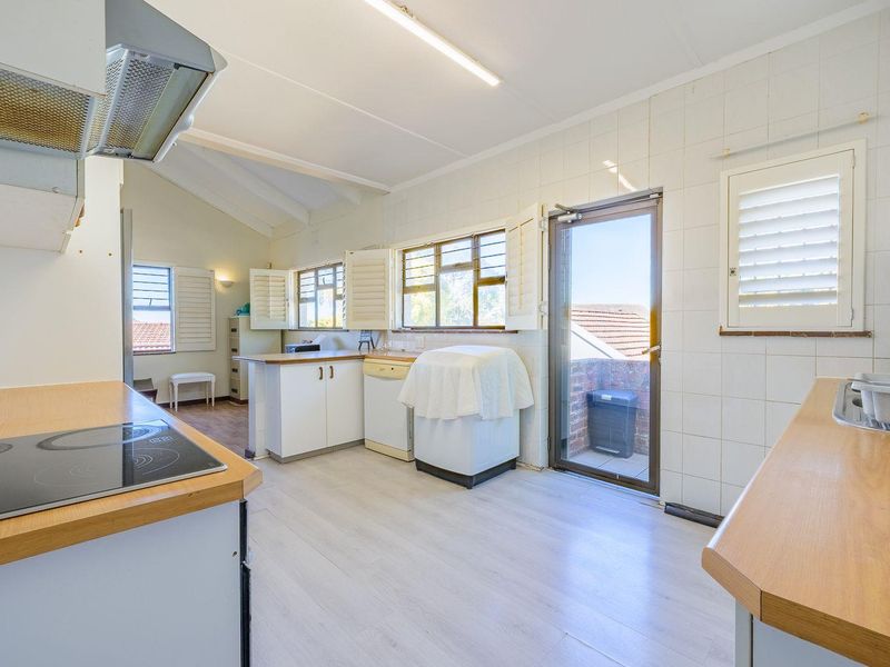 A functional kitchen featuring laminate countertops, an electric cooktop, extractor fan, and direct access to an outdoor area through a glass panel door.