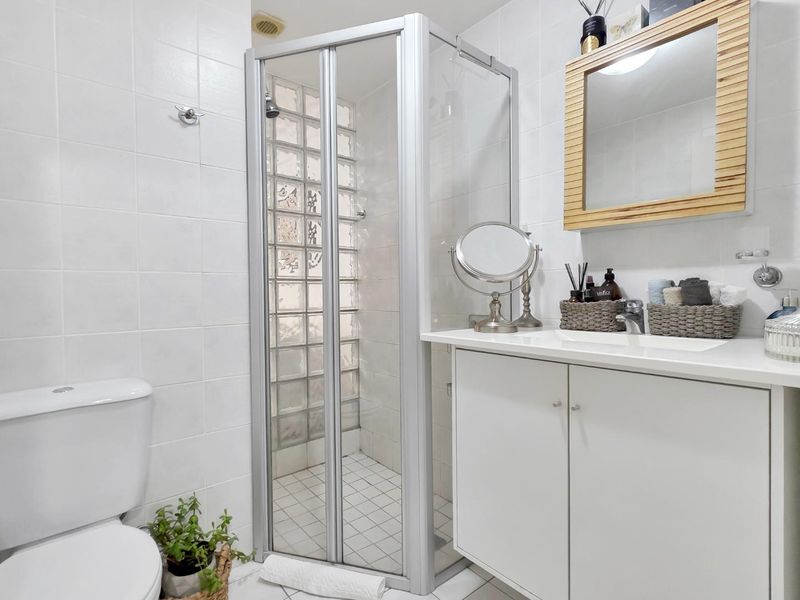 A clean, functional bathroom featuring a shower enclosure with glass block detailing, a white vanity cabinet with integrated sink, and a standard toilet.