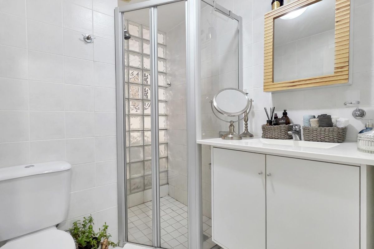 A clean, functional bathroom featuring a shower enclosure with glass block detailing, a white vanity cabinet with integrated sink, and a standard toilet.