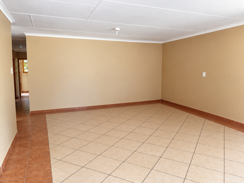 A spacious, empty living area featuring neutral wall tones, ceramic tiled flooring with a decorative border, and a clean coved ceiling.