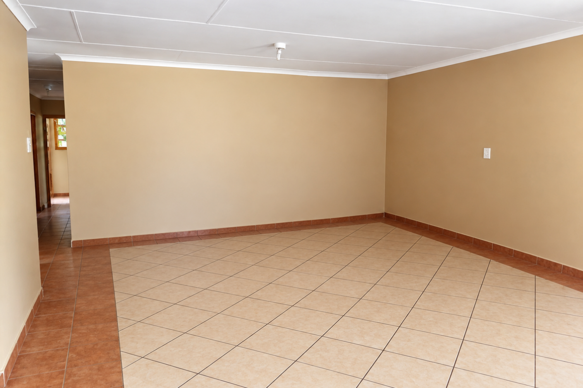 A spacious, empty living area featuring neutral wall tones, ceramic tiled flooring with a decorative border, and a clean coved ceiling.