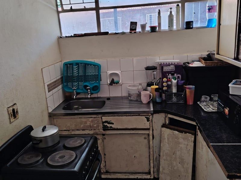 A compact kitchen featuring a stainless steel sink, tiled splashback, and laminate countertops, currently requiring significant cosmetic updates and cabinet repairs.
