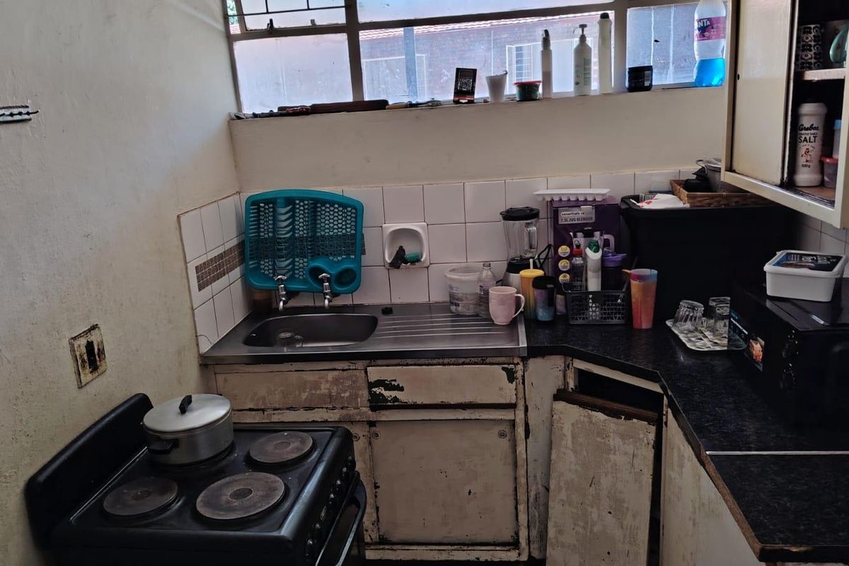 A compact kitchen featuring a stainless steel sink, tiled splashback, and laminate countertops, currently requiring significant cosmetic updates and cabinet repairs.