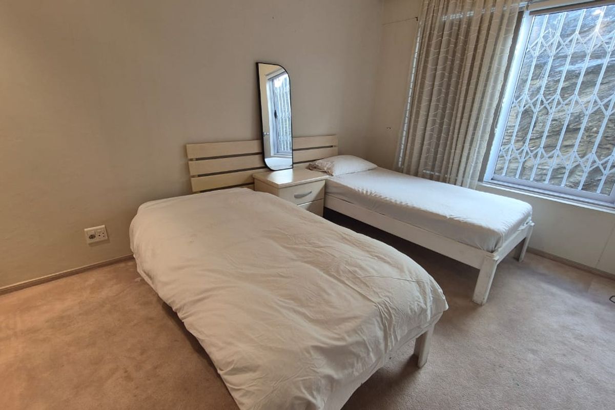 A bedroom featuring neutral wall tones, carpeted flooring, and a window fitted with security bars and curtains.