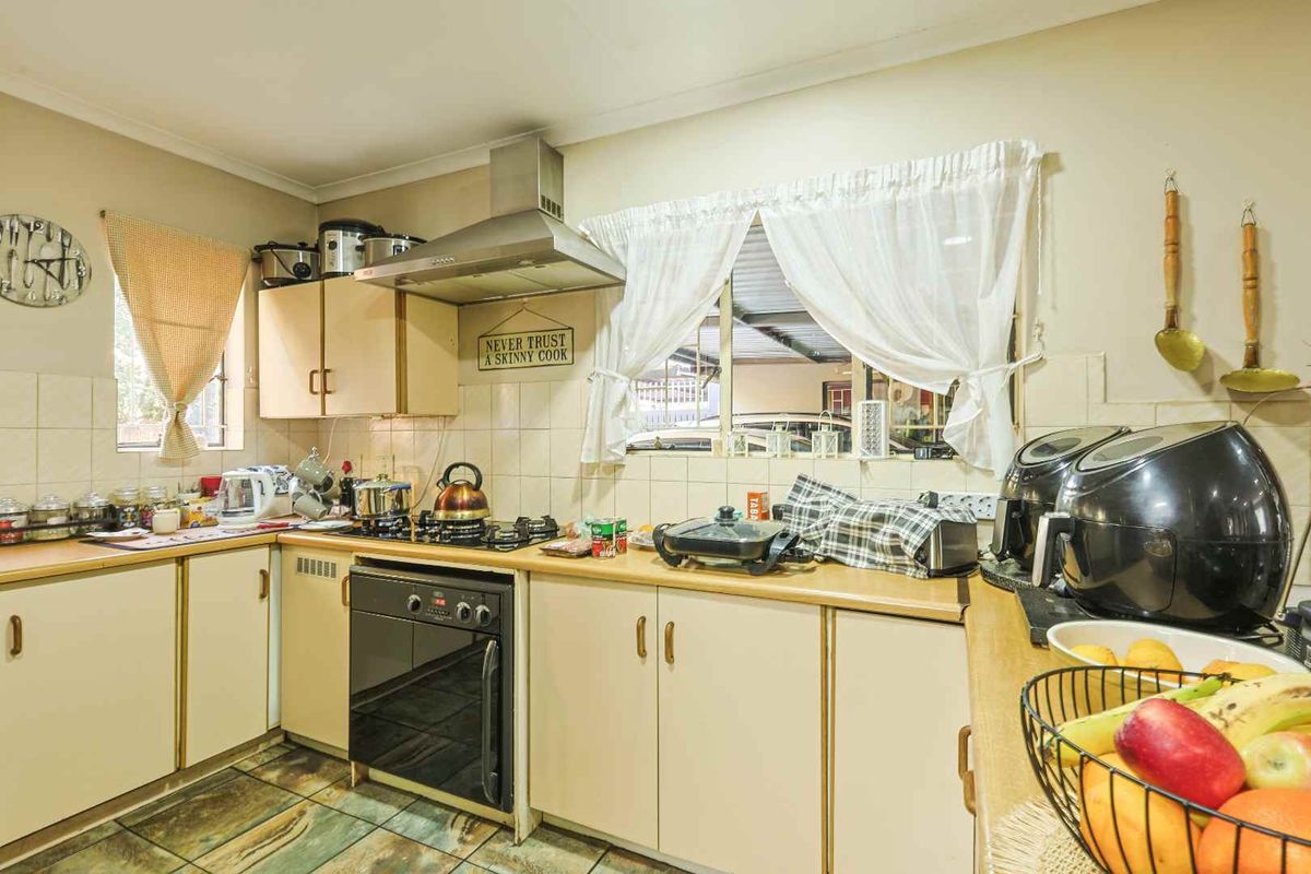 A functional kitchen featuring built-in cabinetry, laminate countertops, a gas hob, and a stainless steel extractor fan with tiled backsplash and flooring.