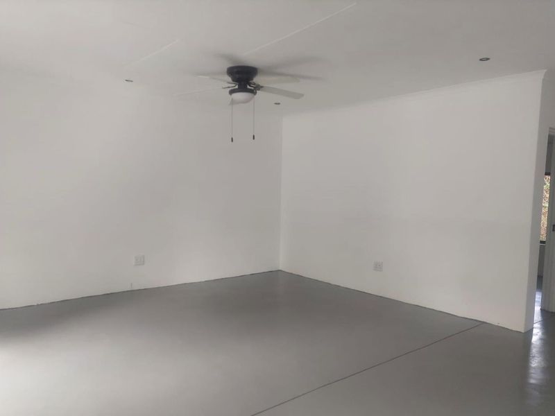 A spacious, empty living area featuring a ceiling fan, recessed lighting, and a clean, painted concrete floor.