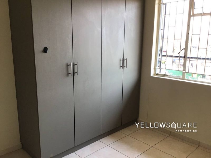 A bedroom featuring built-in cupboards, tiled flooring, and a window fitted with security bars.