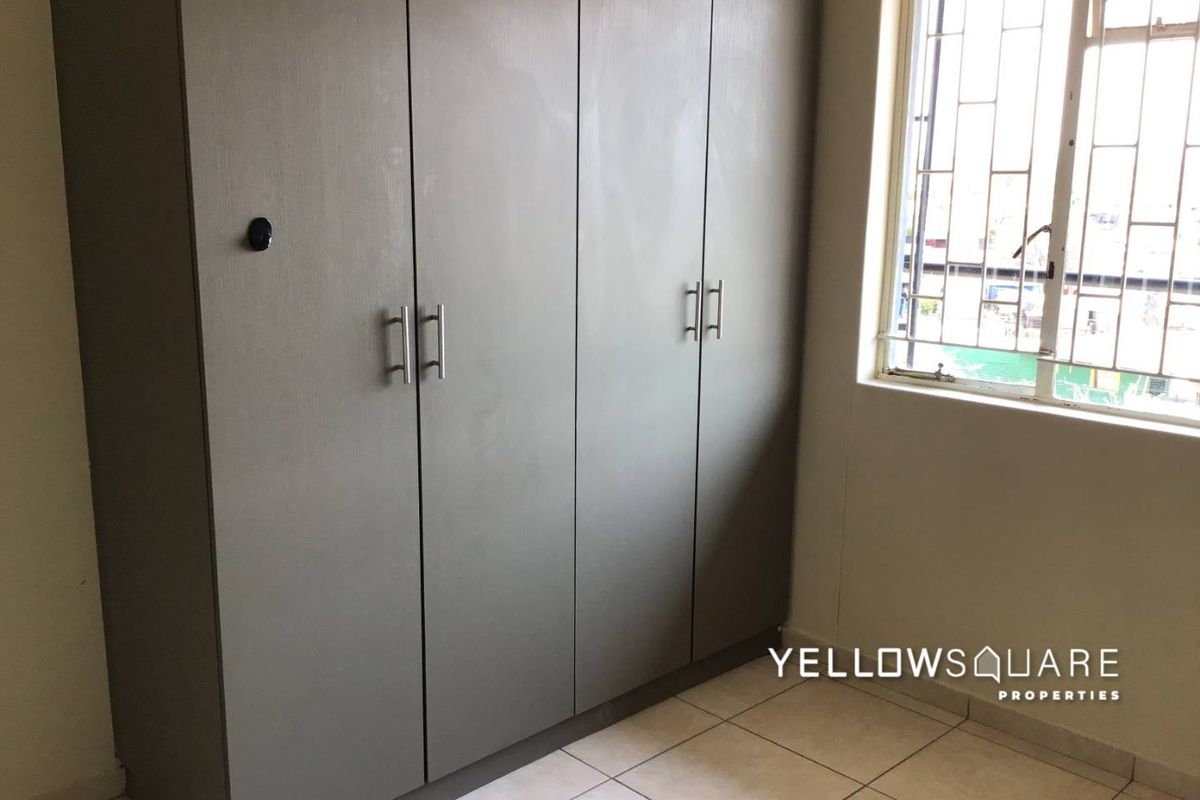 A bedroom featuring built-in cupboards, tiled flooring, and a window fitted with security bars.