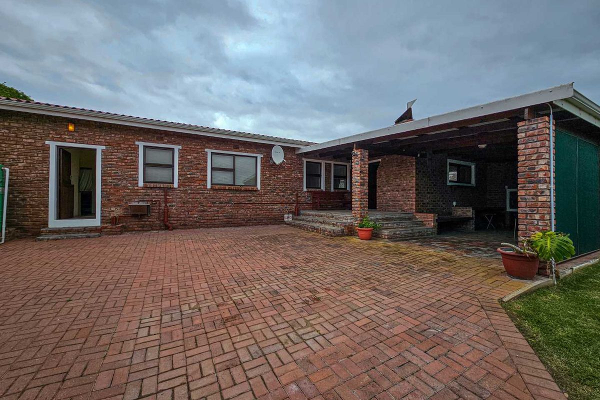Rear exterior view featuring a spacious brick-paved patio area, covered veranda, and exposed brick facade with multiple window access points.