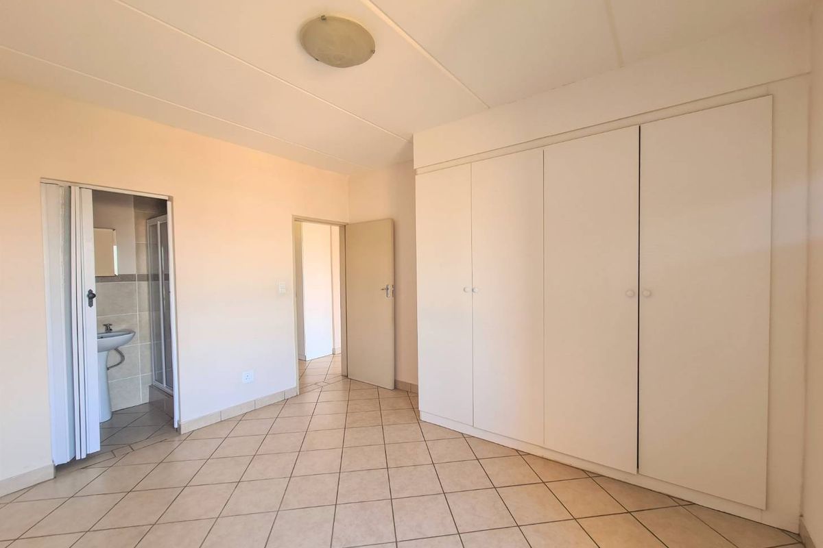 A spacious, empty bedroom featuring neutral tiled flooring, ample built-in cupboard storage, and direct access to an en-suite bathroom.