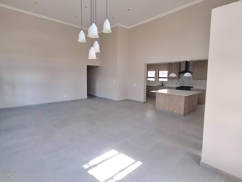 Spacious open-plan living area featuring large format floor tiles, high ceilings, and a modern kitchen with a central island and built-in appliances.
