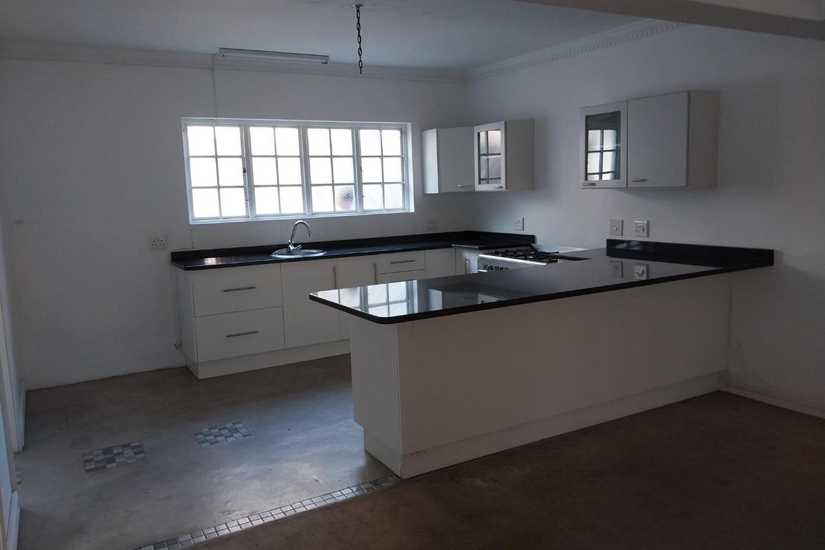 A spacious, empty kitchen featuring white cabinetry, dark granite countertops, a breakfast bar, and a gas hob, ready for final flooring finishes.
