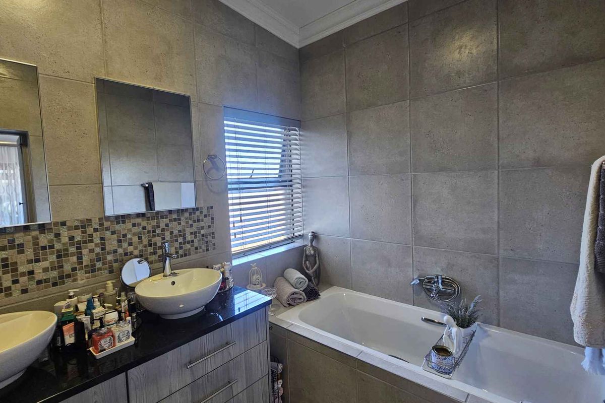 A modern bathroom featuring a double vanity with vessel sinks, granite countertops, and a built-in bathtub with full-height wall tiling.