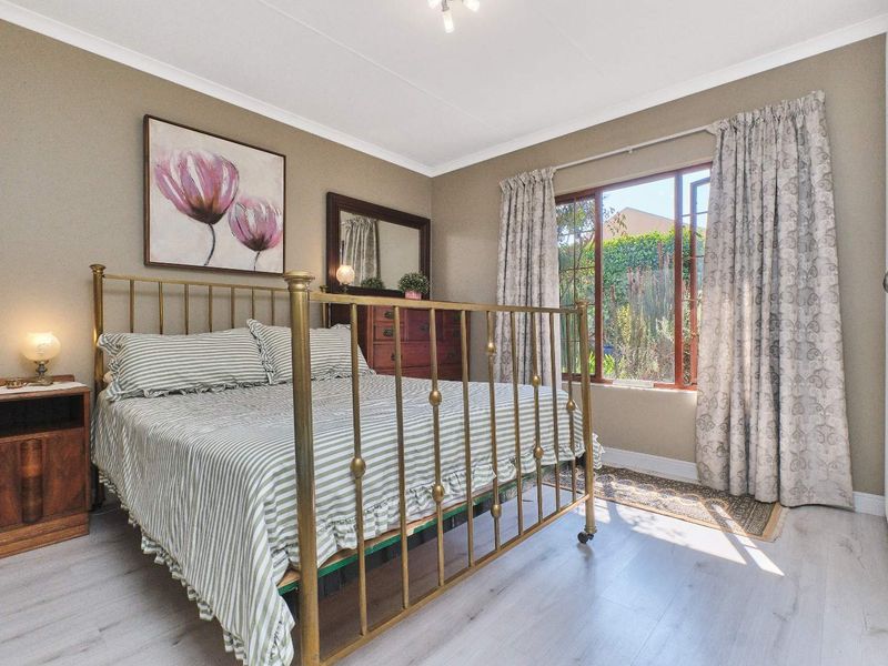 A well-maintained bedroom featuring light-toned laminate flooring, neutral wall paint, and a large window allowing for natural light.
