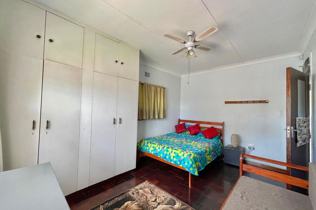 A bedroom featuring built-in floor-to-ceiling wardrobes, a ceiling fan, and dark wood flooring.