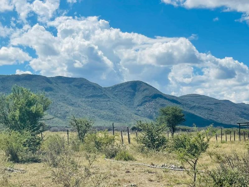 Expansive rural landscape view featuring natural mountain scenery, open grazing land, wire fencing, and a small corrugated metal utility structure.