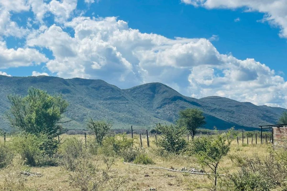 Expansive rural landscape view featuring natural mountain scenery, open grazing land, wire fencing, and a small corrugated metal utility structure.